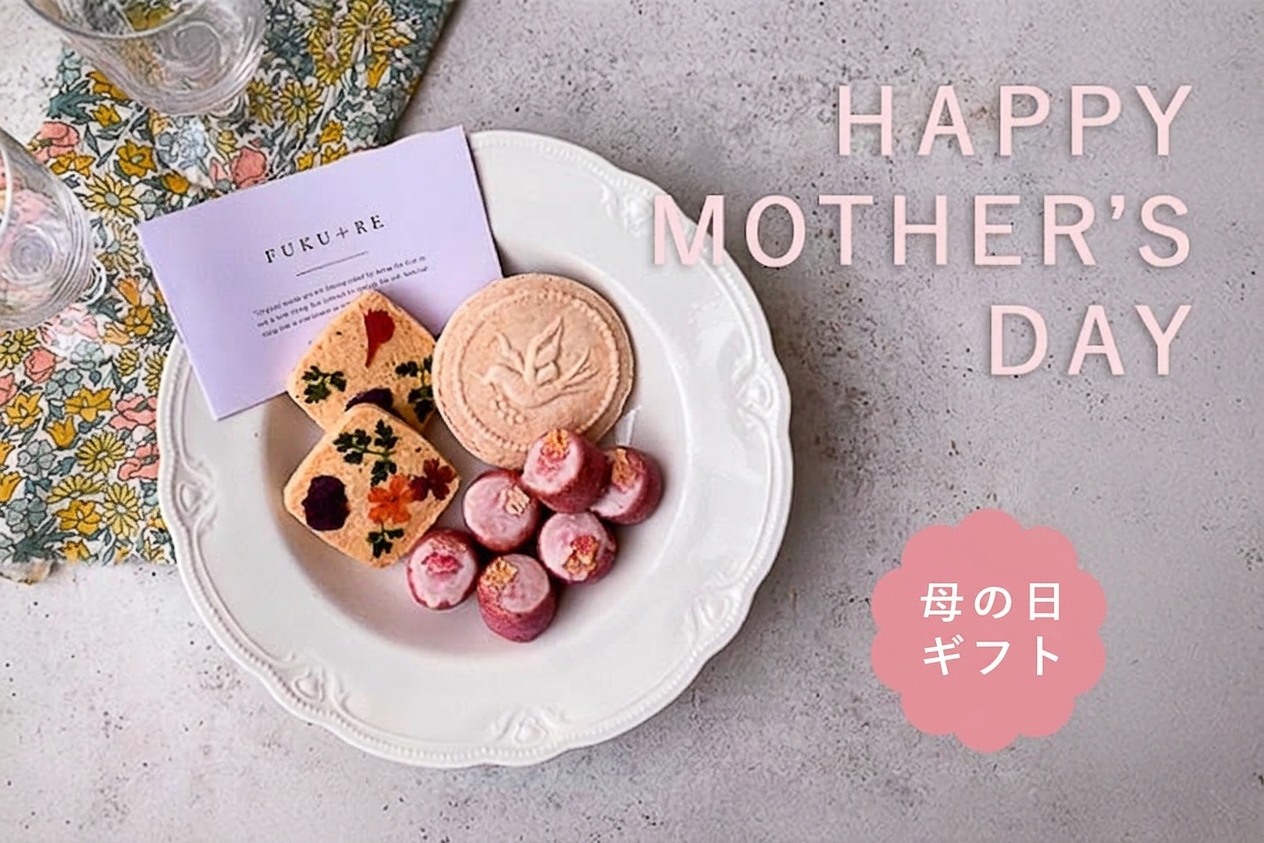 FUKU+REの2026年母の日ギフト特集ページのキービジュアル。鹿児島の郷土菓子ふくれ菓子と焼き菓子の詰め合わせを、母の日のお花とともに俯瞰で撮影した贈り物のシーン