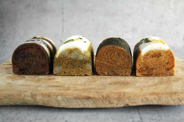 各種の色味と素材を見せる断面。黒糖の濃色、緑茶の緑色、桜島小みかんの橙色、すももを混ぜた深いココア色が鮮やかに広がるプレゼント向け蒸し菓子