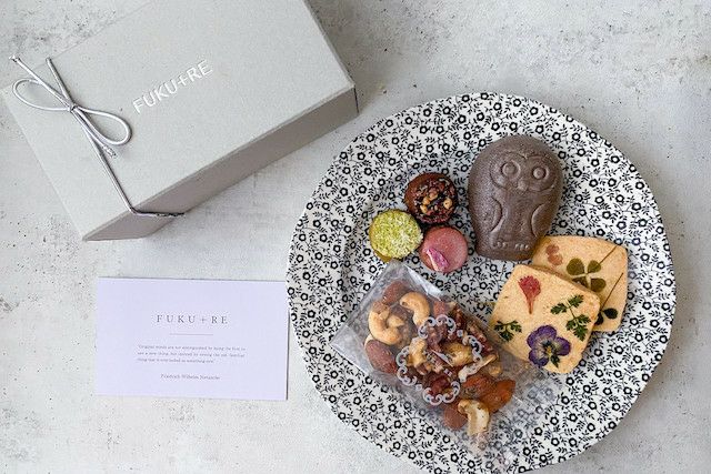 FUKU+REブランドのギフトボックスと、花の押し花クッキー、ナッツ、カラフルな焼き菓子、フクロウ型の和菓子を黒白模様の皿に盛り付けた上品なバレンタインスイーツセットの写真