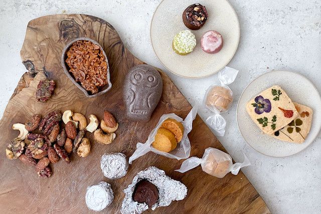 木製のプレートや優しい色の小皿にFUKU+REブランドのギフトボックスと、花の押し花クッキー、ナッツ、カラフルな焼き菓子、フクロウ型の和菓子を盛り付けた上品なバレンタインスイーツセットの写真