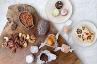 木製のプレートや優しい色の小皿にFUKU+REブランドのギフトボックスと、花の押し花クッキー、ナッツ、カラフルな焼き菓子、フクロウ型の和菓子を盛り付けた上品なバレンタインスイーツセットの写真