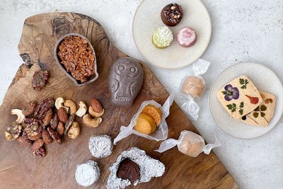 木製のプレートや優しい色の小皿にFUKU+REブランドのギフトボックスと、花の押し花クッキー、ナッツ、カラフルな焼き菓子、フクロウ型の和菓子を盛り付けた上品なバレンタインスイーツセットの写真