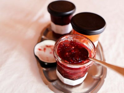 深い赤色のジャムが詰まったガラス瓶の商品写真。開封したジャムからスプーンですくい、上質な色味と際立つ粒感を写している。