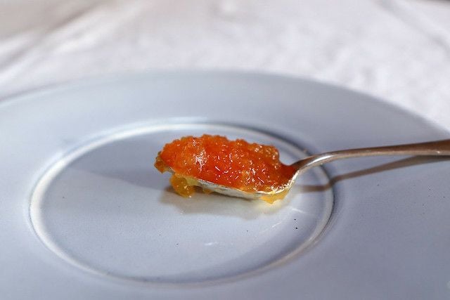 白い皿の上に置かれたスプーンに、鮮やかな橙色のジャムがのっている。粒感が残るジャムの質感が近距離で撮影されている。